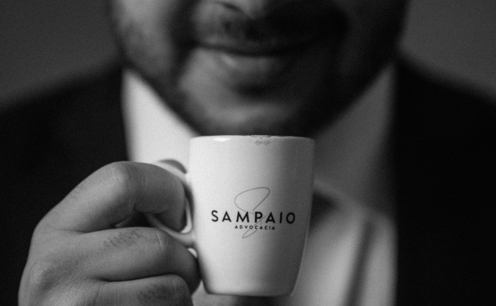 Xícara com a marca Sampaio Advocacia nas mãos de um advogado do escritório